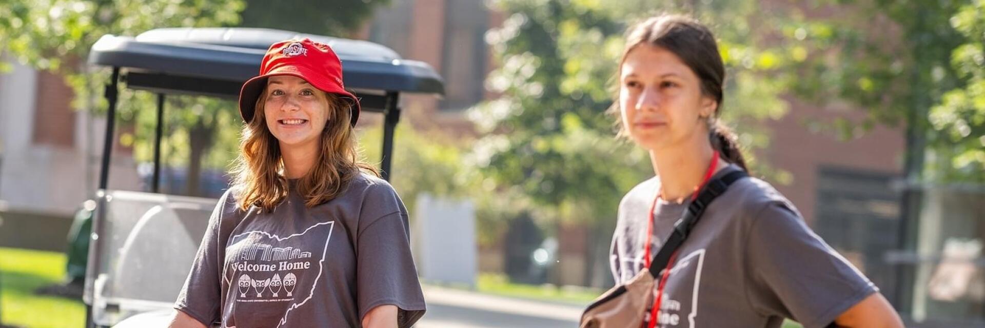 Two OWL Coordinators are helping push a red moving cart, one smiles at the camera